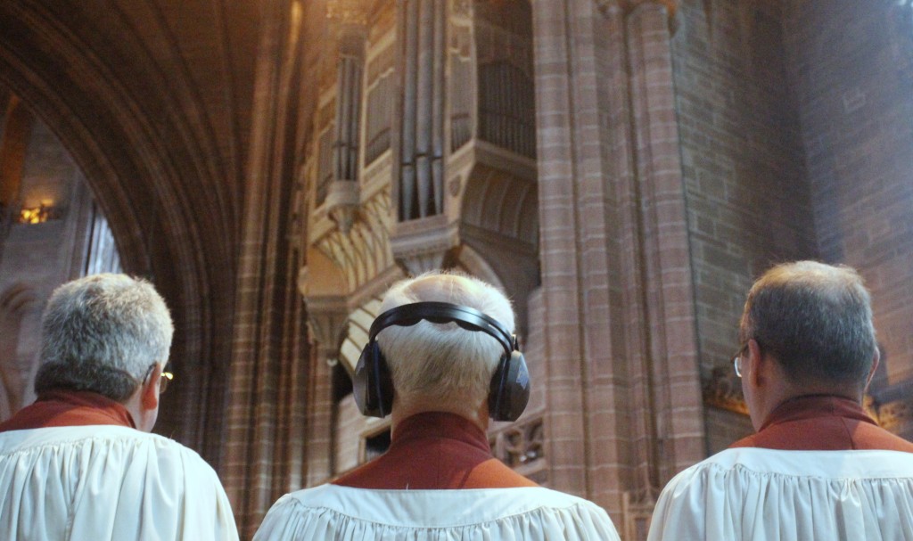 Three singers (one with industrail ear defenders) with a background of the Liverpool Cathedral organ.